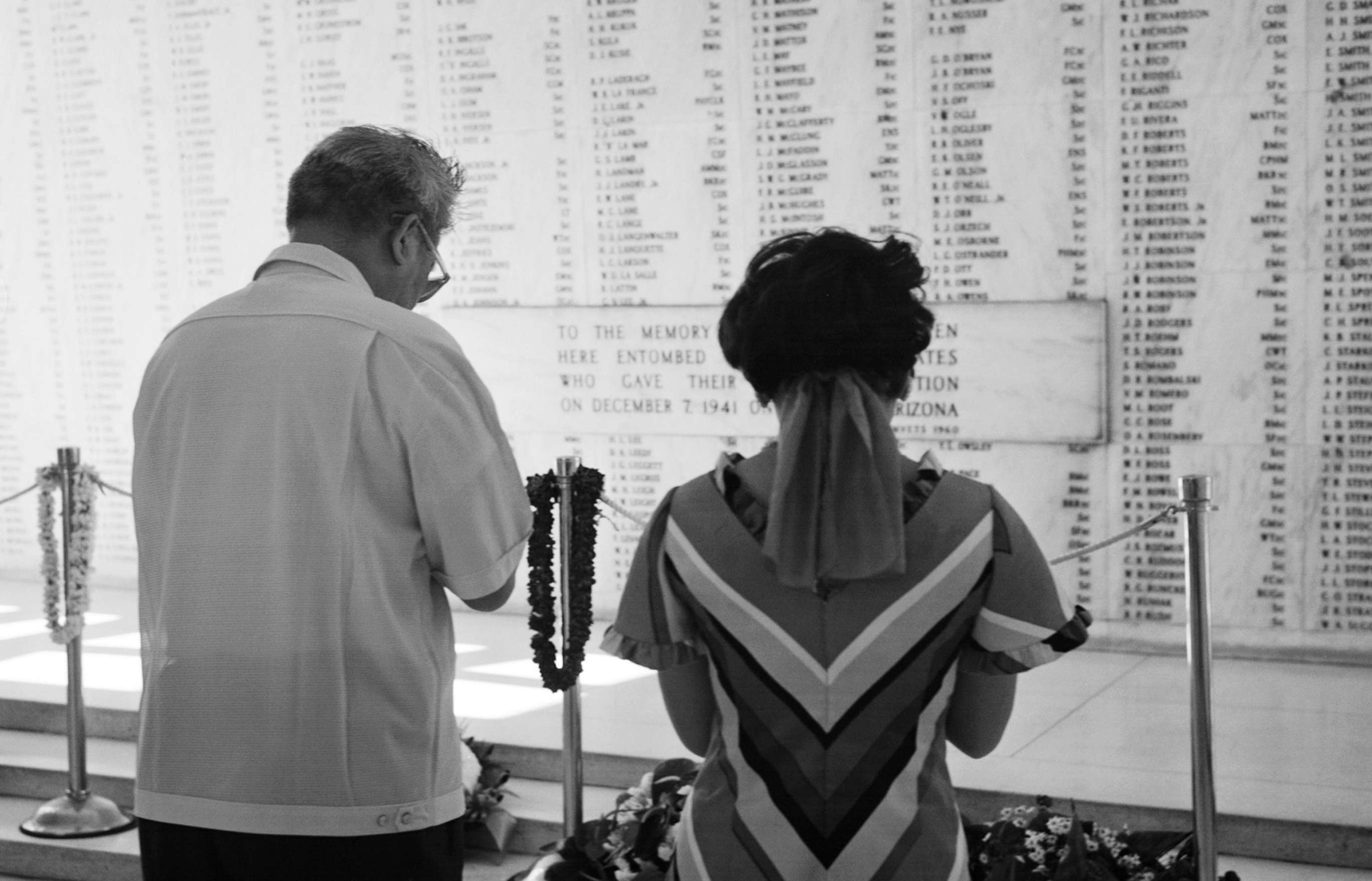 Shinjo and Masako in lay clothes, facing away, bow their heads in prayer before the marble wall of the Arizona Memorial inscribed with the names of the dead at Pearl Harbor.