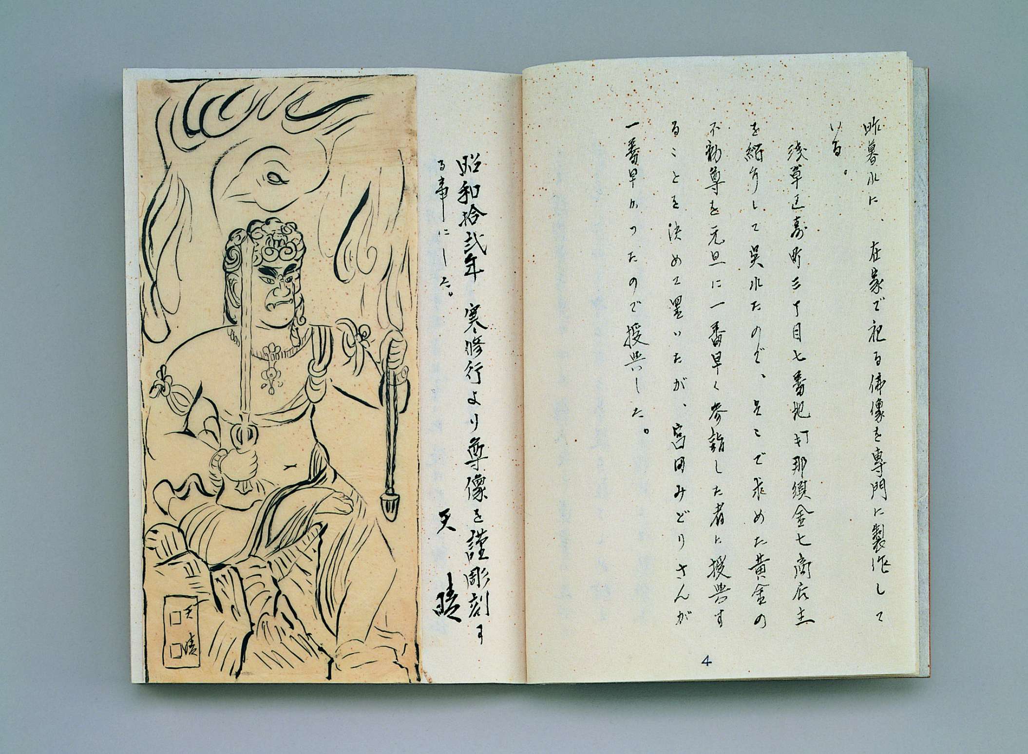 A journal lies open in which a seated scowling figure holding a sword and noose is depicted in black ink on the left page, and vertical columns of Japanese calligraphic writing appear on the right.