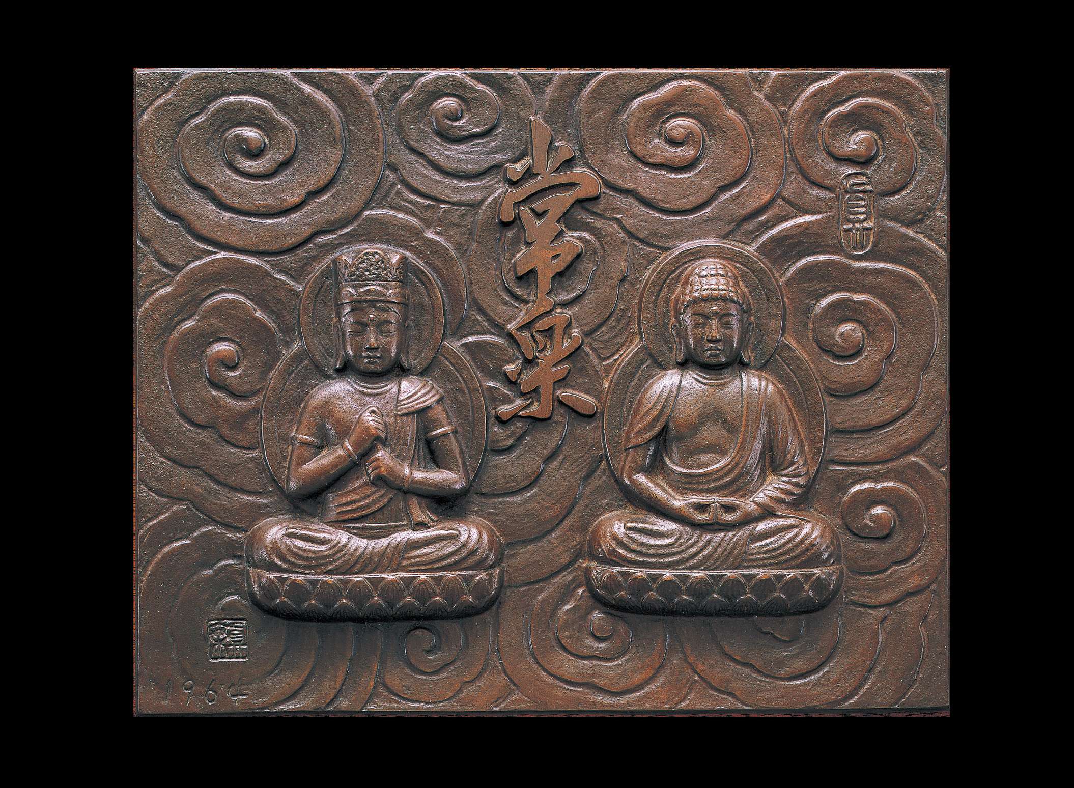 A rectangular dark, metallic relief of two buddhas sitting cross-legged side by side atop lotus seats with raised Japanese calligraphy between them; swirling, stylized clouds form the background.