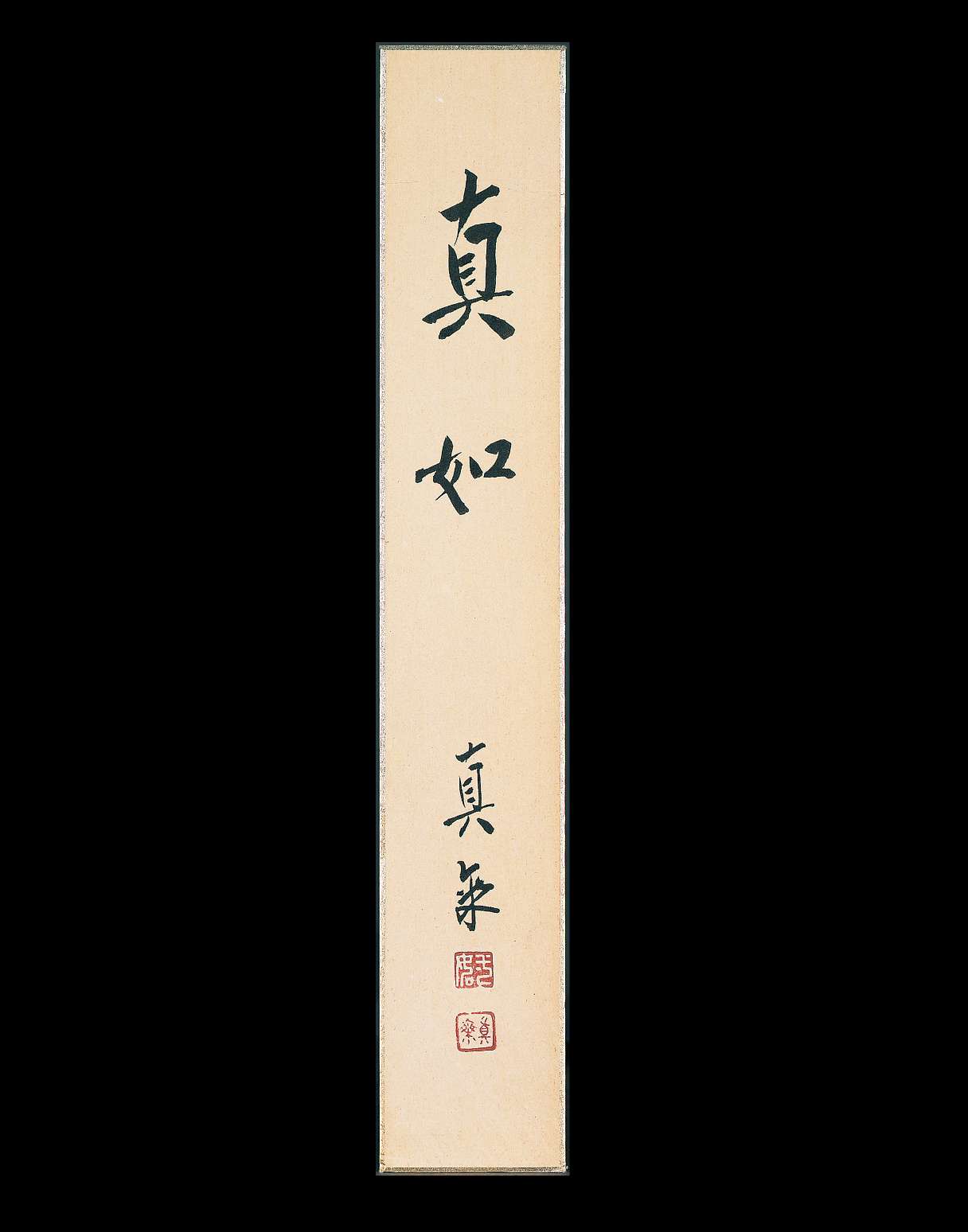 A very long, vertically oriented paper scroll has bold Japanese calligraphy characters written on it in black ink; two square shaped stamps have been impressed on the paper beneath in red.