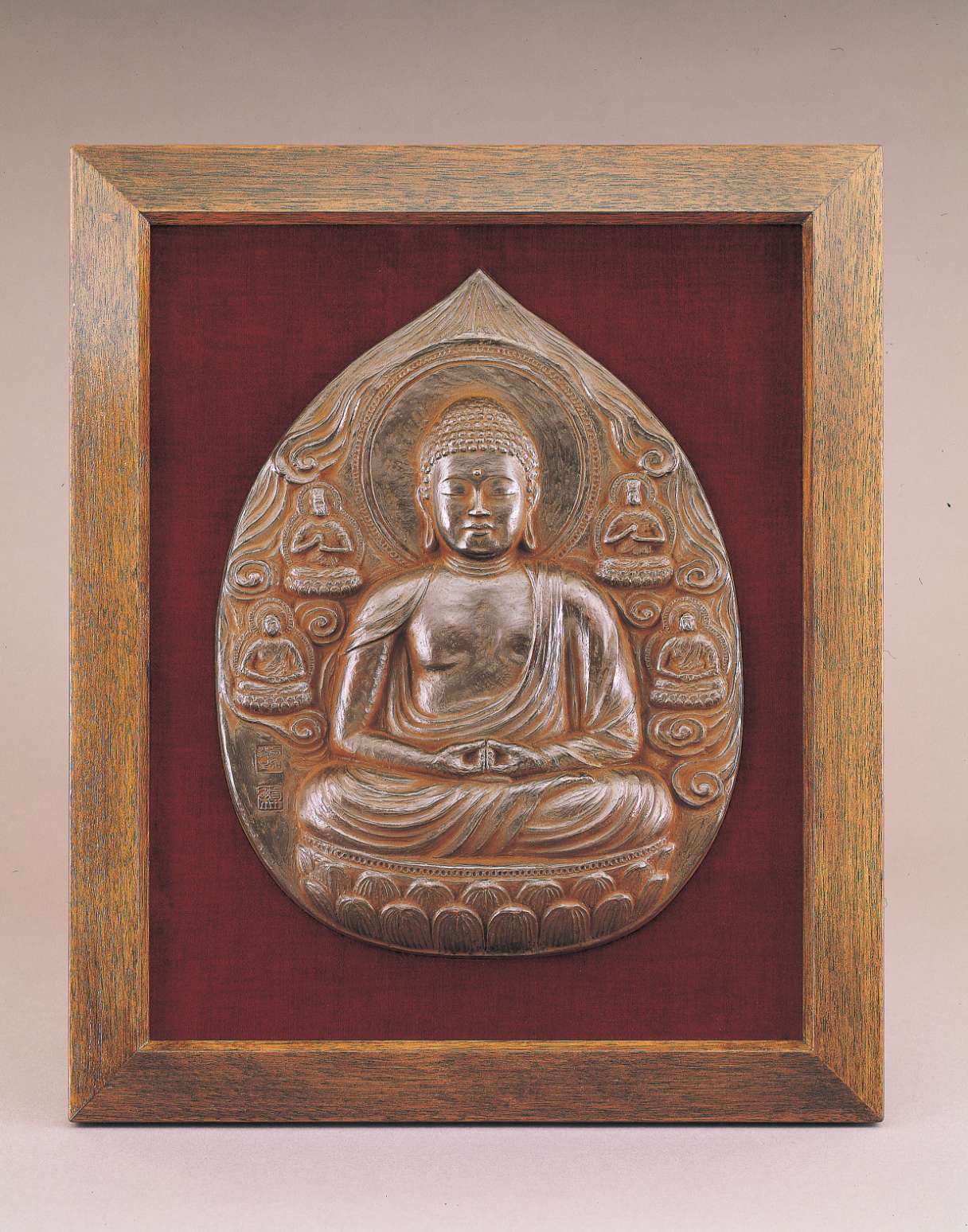 A tear-shaped metallic relief of a buddha sitting cross-legged atop a lotus seat with his hands in meditation posture, surrounded by clouds and four smaller buddhas.