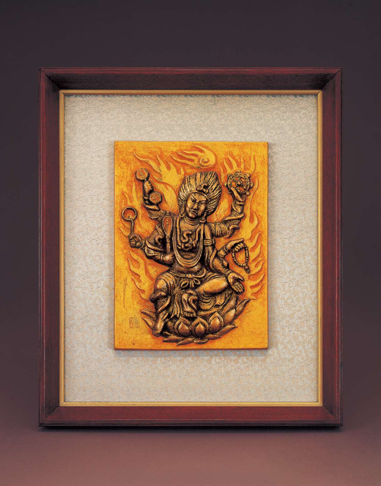A rectangular relief of a scowling six-armed figure with wild windswept hair sitting one leg akimbo atop a lotus seat amid flames; snakes coil on each limb, and the hands wield symbolic implements.